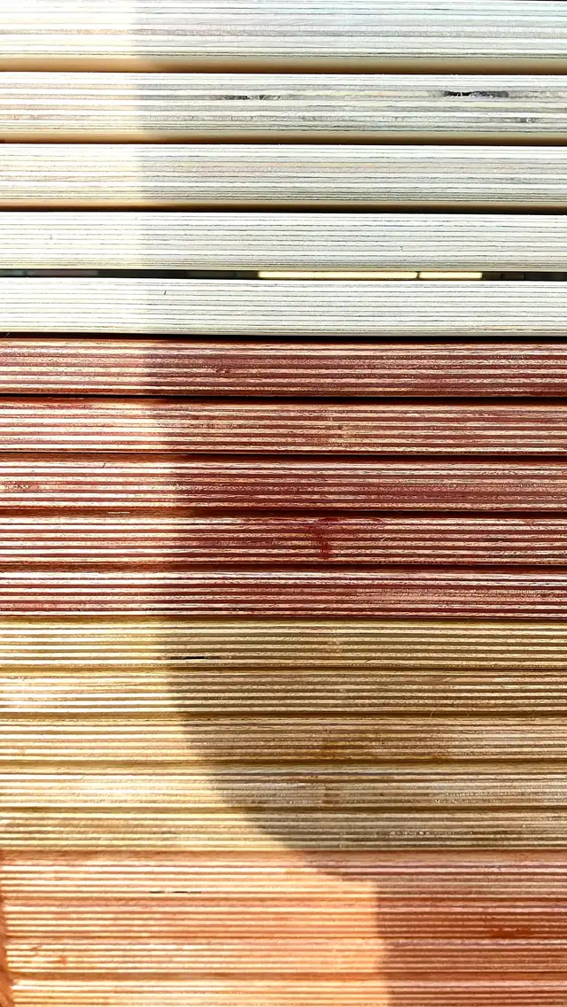 Finished boards stacked edge on in sunlight, showing the run of finishes from pale unstained birch through the warmer and darker stains.