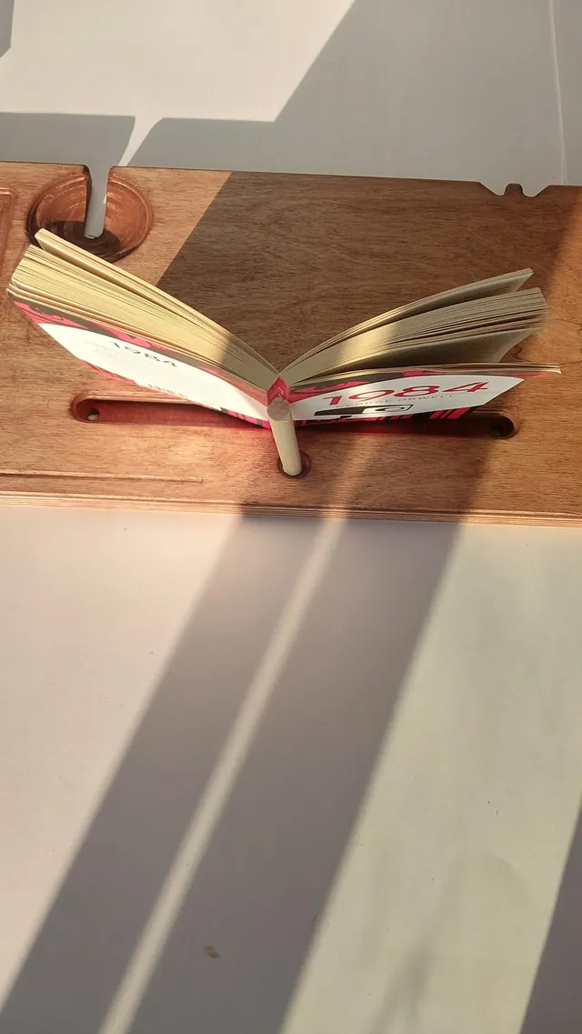 An open paperback standing in the tablet groove, held at the spine by the backstand so both pages stay readable.