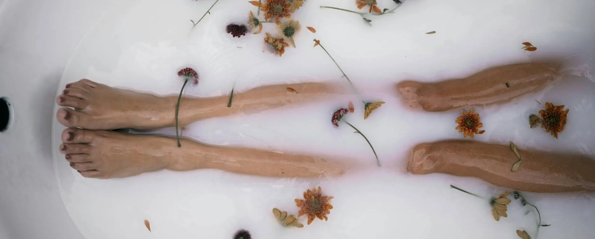 Arms resting in a milky bath scattered with dried flower petals