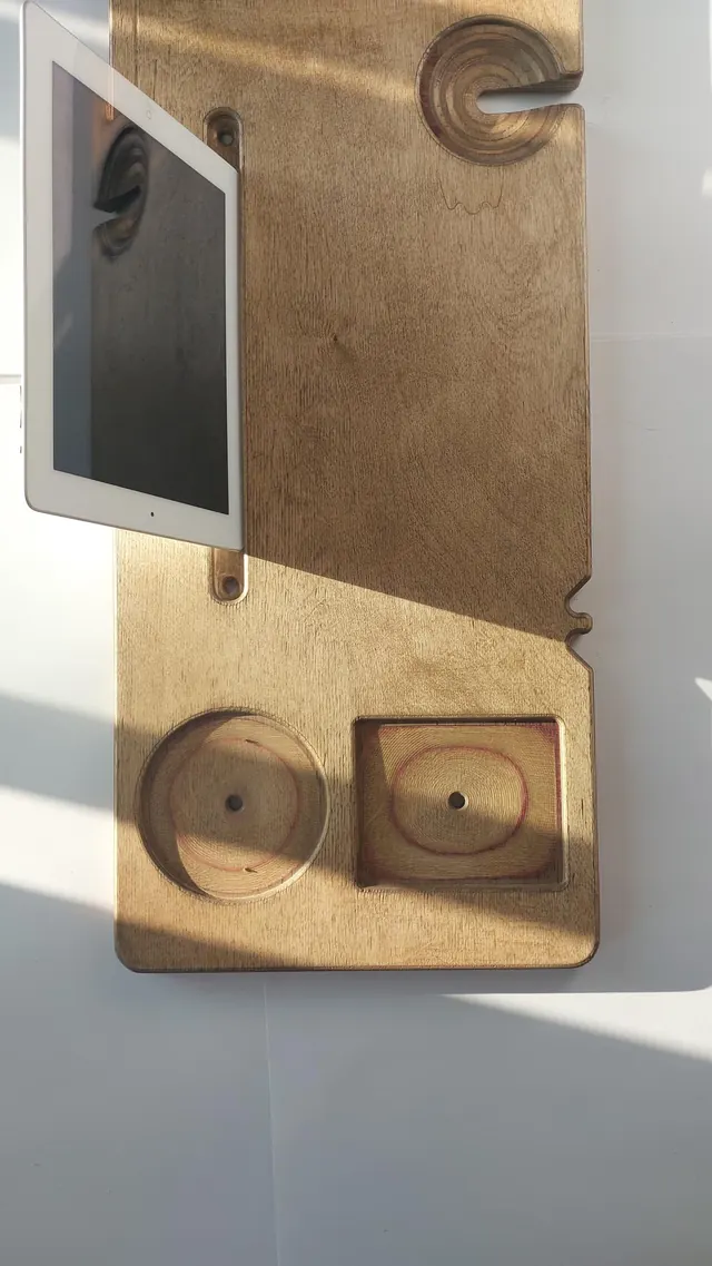 A tablet standing upright in the groove and backstand of a pale board, with the candle holder and square tray on the surface below it.