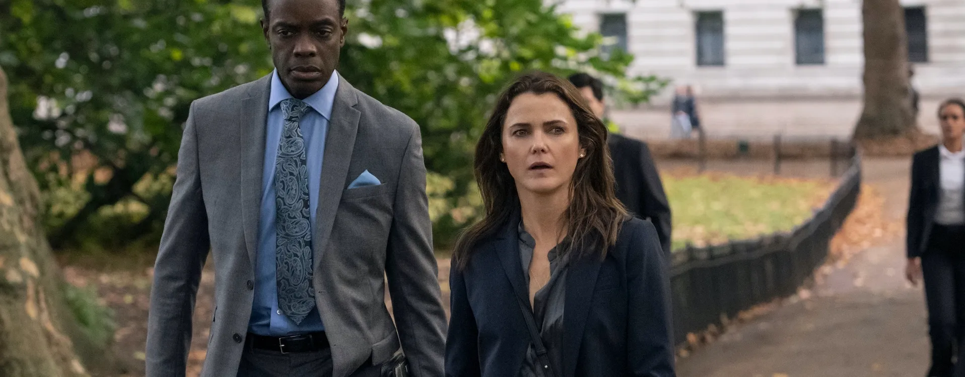 Keri Russell and David Gyasi walking outdoors in suits in The Diplomat